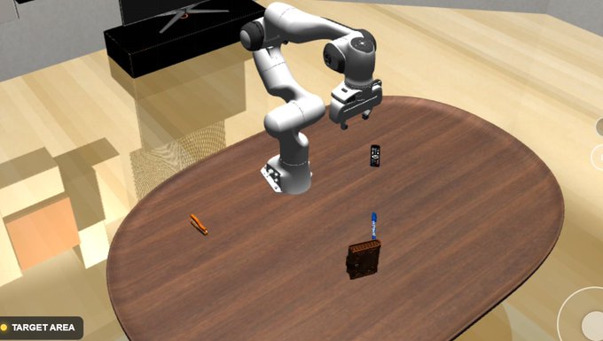 A screenshot from a robot simulation game showing a white robotic arm positioned over a brown wooden table with various objects (an orange rod, a black rectangular item, and a blue pen), with a "TARGET AREA" label visible in the bottom left corner.