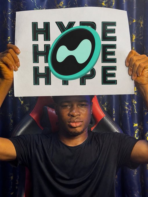 A person holding a sign reading 'HYPE' repeated three times with a teal infinity-like logo, sitting in a gaming chair.