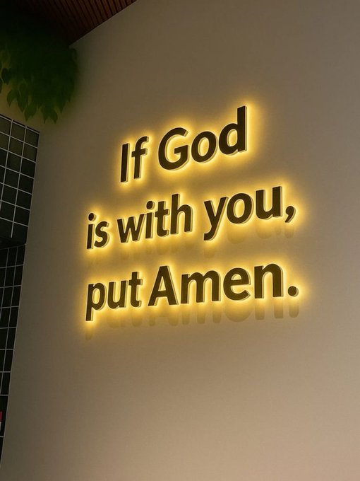 A glowing yellow backlit sign mounted on a wall reads 'If God is with you, put Amen.'