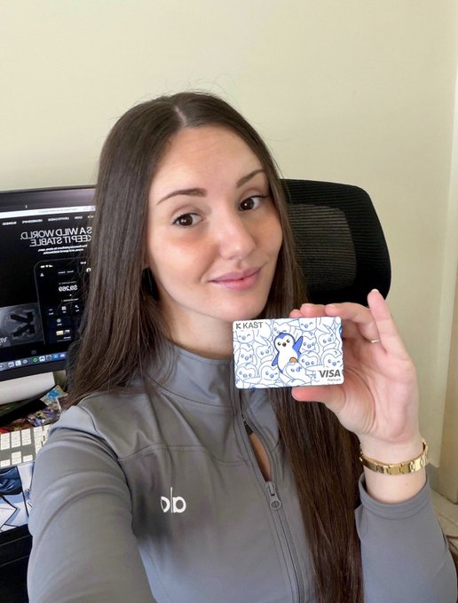 A woman smiles while holding up a physical "KAST VISA" card featuring the iconic Pudgy Penguins penguin design, promoting the giveaway mentioned in the post. Her gray jacket with "dp" logo is visible, alongside a background showing cryptocurrency tools, fitting the context of the Pengu Card spending challenge.