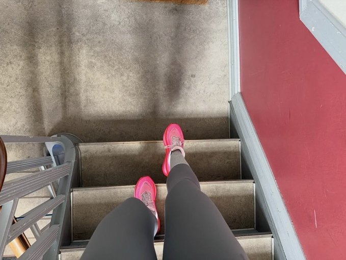 The image shows a person wearing pink sneakers walking up a set of stairs. They are captured from an angle that looks down at their feet as they ascend the stairs. The background features a red wall with a white door, suggesting that this scene takes place in a hallway or entryway to a room. The post accompanying the photo reads "Gm CT pink shoes, morning steps, same mission". This implies that the person is wearing these sneakers for exercise and has chosen to walk up the stairs instead of using an elevator or other means of transportation.