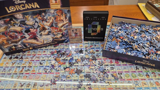 A partially completed Disney Lorcana 1000-piece Ravensburger Puzzle laid out on a table alongside its box, a Disney Lorcana card, and a box of Ricolas Grenadine Renaissance chocolates.
