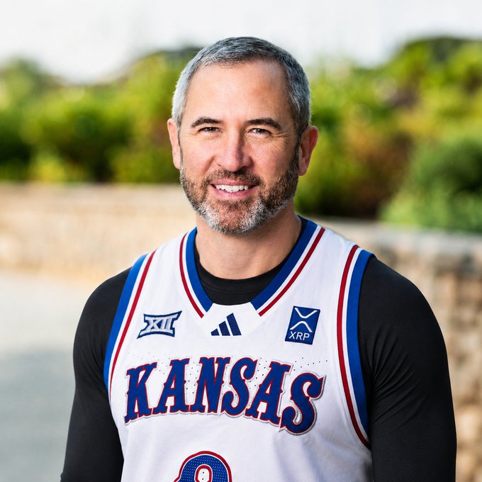 A smiling man with gray hair and a beard poses in a Kansas Jayhawks basketball jersey featuring the Big 12 conference logo, Adidas branding, and an "XRP" sponsor patch. The post tags @bgarlinghouse, suggesting the man is Brad Garlinghouse, the CEO of Ripple (the XRP-connected blockchain company), shown here in Kansas team apparel.