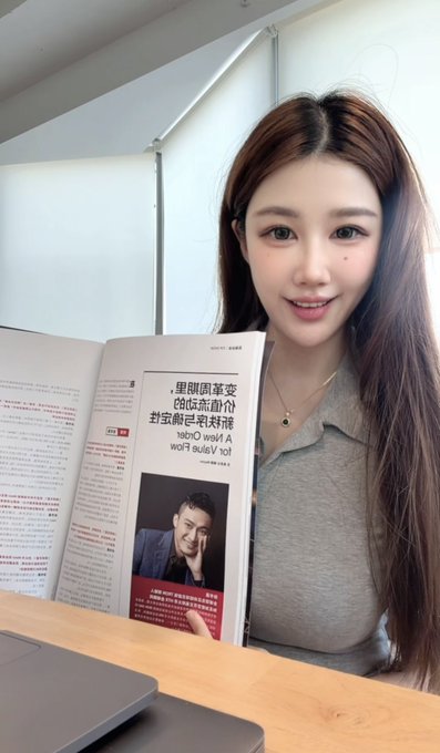 A young woman smiles while holding an open magazine at a desk, with the visible page showing a photo of actor Jackie Chan and Chinese text including '我就 A hot wolf' and 'A·欢快我于' (...)