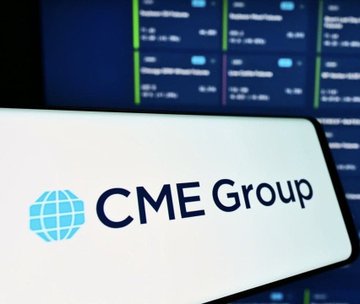 A smartphone displays the CME Group logo and name in front of a blurred financial data screen.
