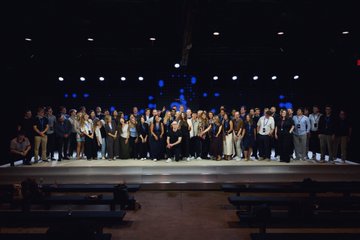 The image features a large group of people standing together for a photo at an event. They are all dressed up and posing for the camera, with some individuals holding microphones or other equipment. The background shows a stage set up with lights, indicating that this is likely a formal gathering or performance. The post includes text about Coinbase employees celebrating their hard work and dedication in making announcements possible during the Bitcoin exchange's IPO.