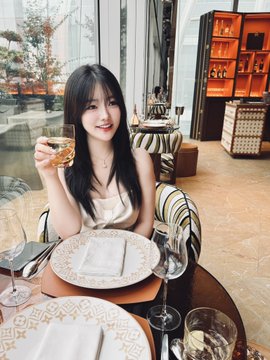 A young woman with long dark hair smiles while holding a glass at an elegantly set dining table in a sophisticated venue with striped chairs and a display cabinet in the background. The post expresses excitement about winning an Apple Watch from the @binancezh "Best Entrance Style Award" at the fifth #BinancePeripheralAmbassador event, with the image capturing her celebratory dinner moment.