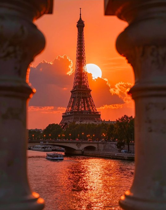 A scenic photograph captures the Eiffel Tower silhouetted against a vibrant orange sunset, framed by two ornate white columns in the foreground, with the Seine River and boats below.