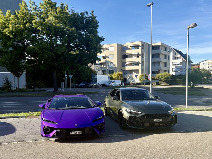 A vibrant purple Ferrari sports car is parked next to a sleek black Toyota sedan, both displaying license plates "ZH-938-VT" and "ZH-264-GT," against a backdrop of modern apartment buildings and trees.