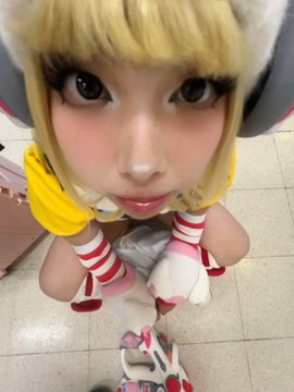 The image shows a cosplayer in a yellow and white outfit with striped socks, crouching down to give the camera a close-up, wide-eyed "fish-eye" perspective. The accompanying text "JUNO 1HP🫪" humorously suggests the character is at their last hit point in a video game, matching the dramatic, vulnerable pose of the cosplayer.