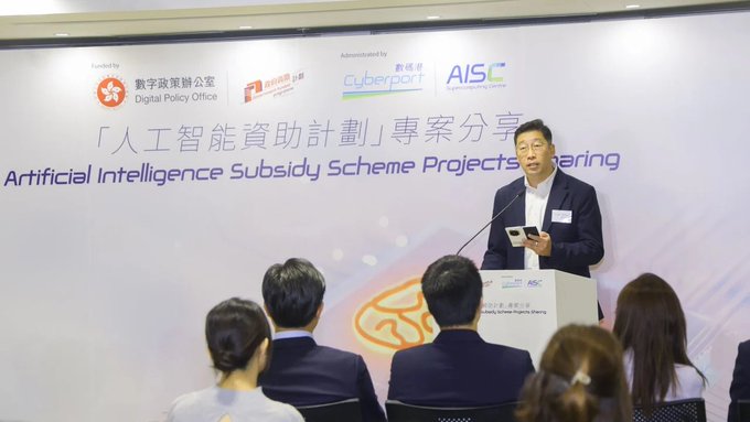 A man speaks at a podium during an event about the Artificial Intelligence Subsidy Scheme Projects Sharing, with logos for the Digital Policy Office and Cyberport visible.