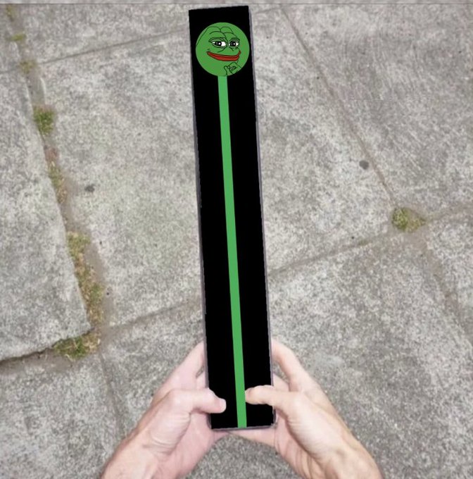 Two hands hold a tall, elongated black box decorated with a green vertical stripe and a Pepe the Frog face on a concrete surface.