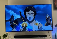 A television displaying an animated character in blue and gold armor holding a glowing blue gem, with other figures visible in the background.