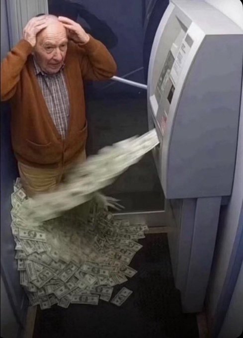 An older man in an orange cardigan stands with hands on his head in disbelief as an ATM machine spews out a massive pile of US dollar bills onto the floor.