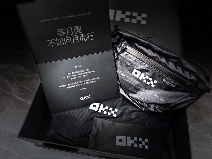 A black gift box containing OKX-branded merchandise including a pouch, drawstring bag, and a card with Chinese text 'HAPPY MID-AUTUMN FESTIVAL' and '等月圆 不如向月而行'.