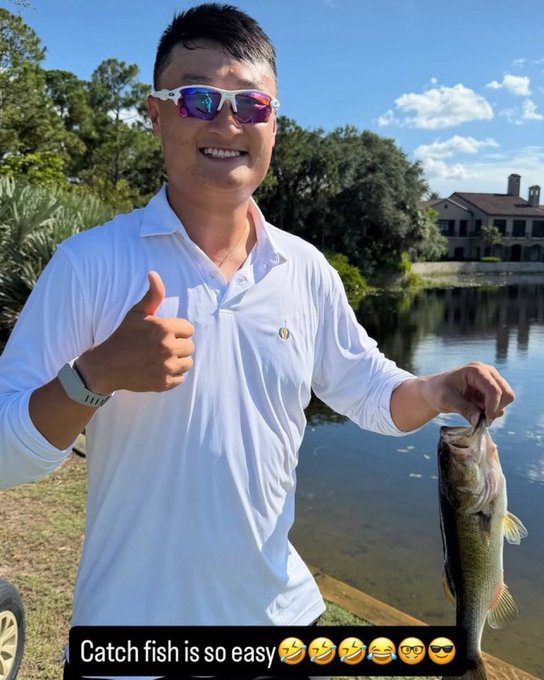 A smiling man in a white polo shirt and sunglasses gives a thumbs-up while holding up a caught bass fish by the lake, with the caption "Catch fish is so easy" followed by laughing emojis, cleverly playing on the post's boast about being "Bottom on the torta token $mamAOCita" by humorously equating an easy fish catch to an easy financial loss.