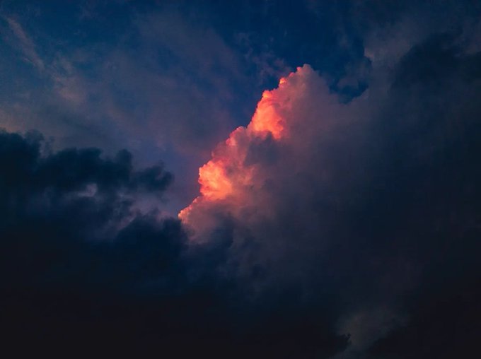 A dramatic cloudscape at dusk with a single pink cloud illuminated against a dark, moody sky.