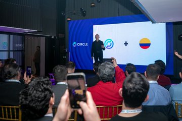 A speaker presents on stage in front of a screen displaying the "CIRCLE" logo and the Colombian flag, addressing an audience whose attendees are capturing the moment on their phones at an event in Bogotá. The image visually aligns with the post's message of Circle's expanding engagement with banks, fintechs, and crypto exchanges in Colombia.