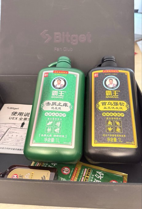 The image shows two bottles of shampoo, one green and one black, placed inside a box with other items such as a book and some papers. The text "用 @bitget 炒美股", which translates to "use bitget", is visible in the image. This suggests that the shampoo might be related to Bitget or could potentially be a product of their brand.