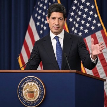 A man in a suit standing at a podium bearing the U.S. House of Representatives seal, speaking in front of American flags.