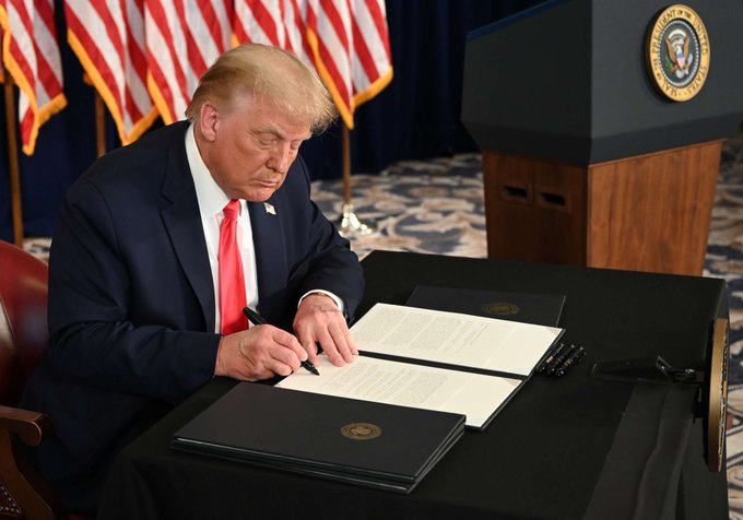 Former President Donald Trump is seen signing a document at a desk featuring the presidential seal, with American flags in the background, symbolizing political promises that the accompanying text suggests are failing the crypto industry as the Clarity Act's odds of passing drop from 70% to 44%.