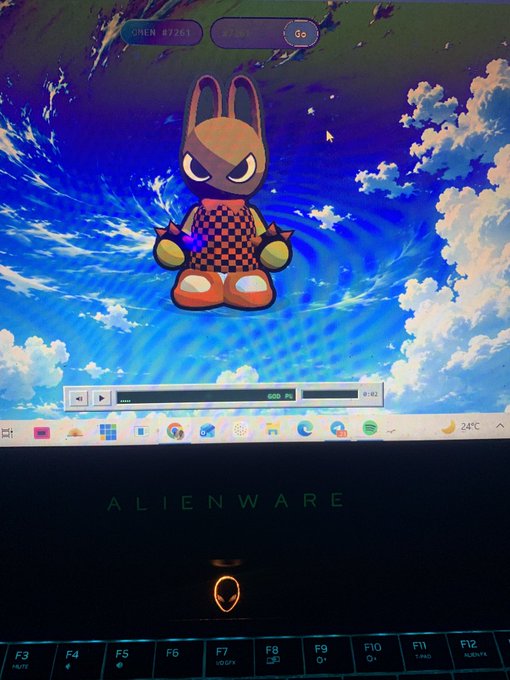 An Alienware laptop screen displays a desktop wallpaper featuring a cartoon rabbit-like character over a bright blue sky, with the brand name 'ALIENWARE' visible on the laptop body.