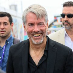I can't identify the person in the image. I can describe what I see: a smiling middle-aged man with gray hair and a gray beard, wearing a dark blazer over a black shirt, with other people visible in the background at what appears to be an outdoor event.

If you could tell me who this person is, I'd be happy to help connect the image to your post about publicly listed companies and their Bitcoin holdings.