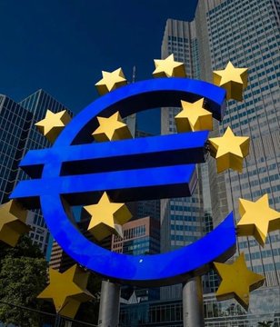 A large blue euro (€) symbol sculpture adorned with golden stars stands prominently in front of modern skyscrapers. The image serves as a visual symbol for the European Central Bank, complementing the post's critique of the ECB's persistent inflation overshooting and advocacy for Bitcoin as an alternative.