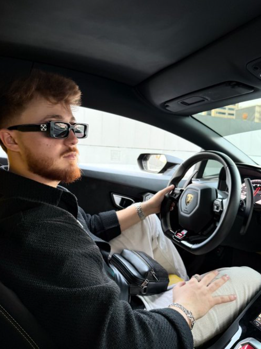 MrBeast, sporting distinctive Off-White sunglasses, sits behind the wheel of a Lamborghini, embodying the "gms" (gas money standard) lifestyle often associated with his flashy brand persona.