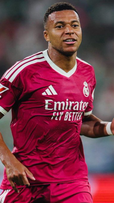 A Real Madrid player wearing the team's maroon away kit smiles during a match, with the jersey displaying the "Emirates FLY BETTER" sponsor and the club crest, visually tying into the post about Real Madrid's diminished LaLiga title chances following their loss to Real Betis.