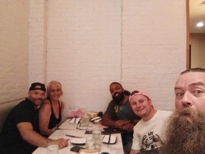 A group of five people posing for a selfie at a restaurant table, including a man with a long beard in the foreground.