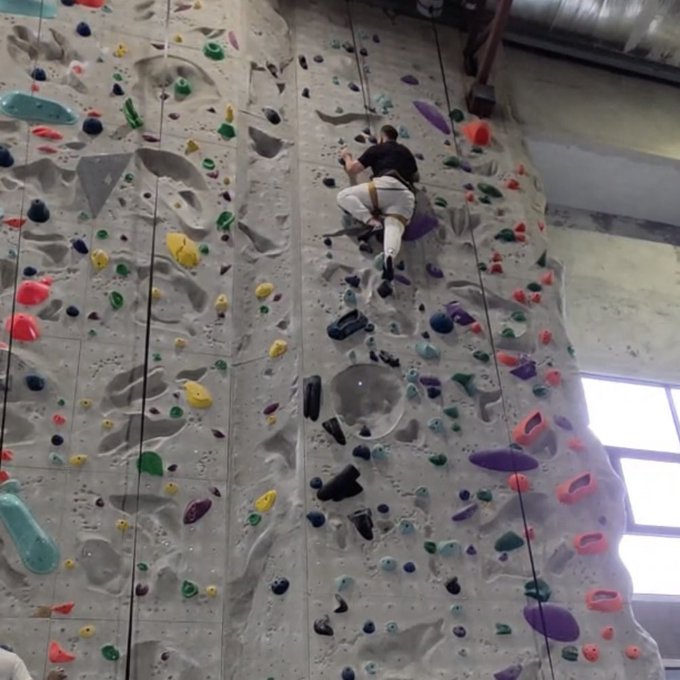 A person scales an indoor rock climbing wall covered with colorful handholds.