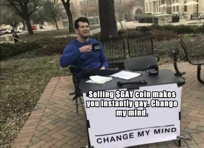 A man sits at a table outdoors behind a 'CHANGE MY MIND' sign with the caption 'Selling $GAY coin makes you instantly gay. Change my mind.'