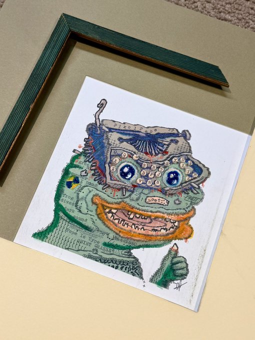 A colorful hand-drawn illustration of a quirky, wide-eyed green character with a large toothy grin is displayed next to its green wooden frame on a tan surface.