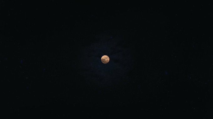 A photograph of a blood moon visible in a dark night sky filled with faint stars.