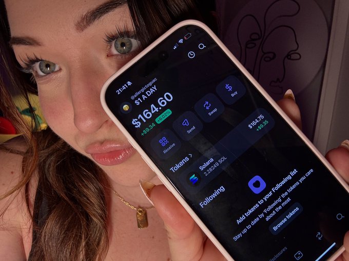 A woman holds up her phone displaying a Solflare wallet showing a balance of $164.60 from her "$1 A DAY" challenge, with a Solana (SOL) holding of 2.8343 tokens worth $164.75 (+$3.35), visually documenting day 219 of her daily $1 SOL accumulation.