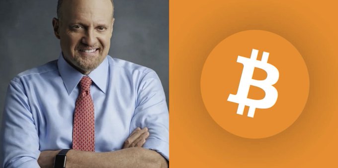 A portrait of a smiling, bald man in a blue shirt and red tie with his arms crossed, shown next to a large orange Bitcoin (₿) logo on an orange background.
