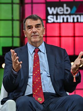 Former UK Prime Minister Gordon Brown speaks animatedly with open hands, wearing a dark suit and a red tie with yellow dots, at the 'Web Summit' conference.