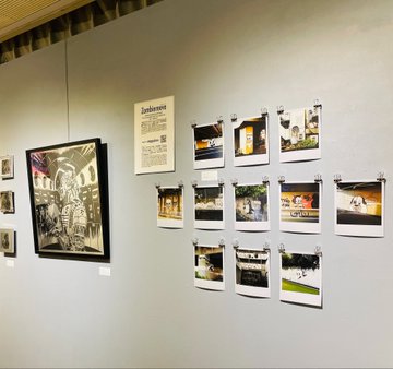 A gallery wall displays various photographs and prints mounted with clips, alongside a framed artwork on the left.