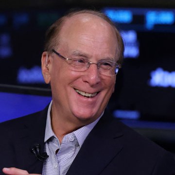 A smiling older man with glasses, wearing a dark blazer over a light blue shirt, appears to be at a media event with screens in the background. The image likely depicts Larry Fink, CEO of BlackRock, whose firm is mentioned in the post as having ETF clients that purchased $183.66 million worth of Bitcoin ($BTC), signaling a resurgence of institutional crypto investment.
