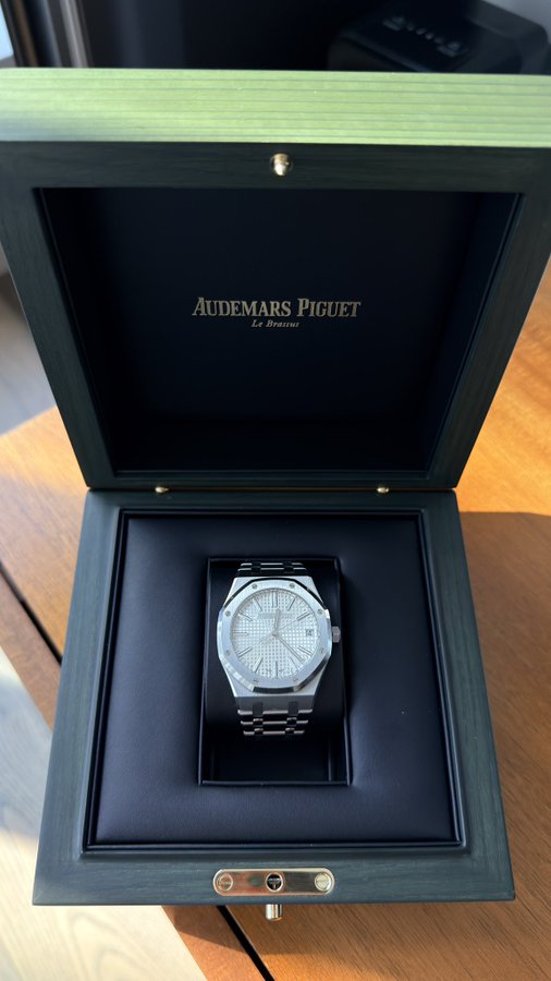 An Audemars Piguet luxury watch displayed in its dark green presentation box, featuring a stainless steel bracelet and a textured silver dial.