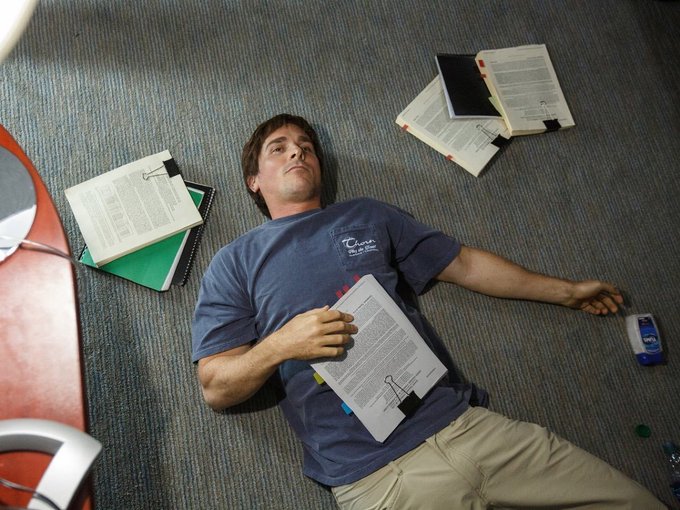 A man in a blue 'Cato Institute' t-shirt lies on a carpeted floor surrounded by scattered open binders, notebooks, and papers in what appears to be an office setting.