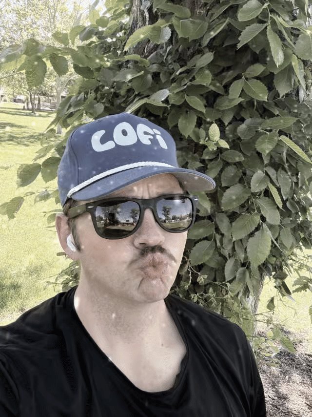 The image features a man wearing sunglasses and a cap with the word "Cofi" written on it, standing next to a tree. The man has a mustache and appears to be making a funny face or smirk for the camera. The background of the photo is blurred, but there are trees visible in the distance. The image also contains text that reads: "Web3 changes fast, but $LOFI is doubling down on what it can control: Community  60K+ members  Major charity impact (220k+)  Onboarding the masses to $SUI Overall, @lofitheyeti is strongly becoming a top brand and making real world change".