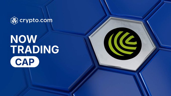 Crypto.com announcement graphic featuring its logo and the text "NOW TRADING CAP" alongside a green circular emblem on a blue hexagonal background, promoting the availability of the CAP token ($CAP) for trading on its platform with support for multiple fiat currencies.