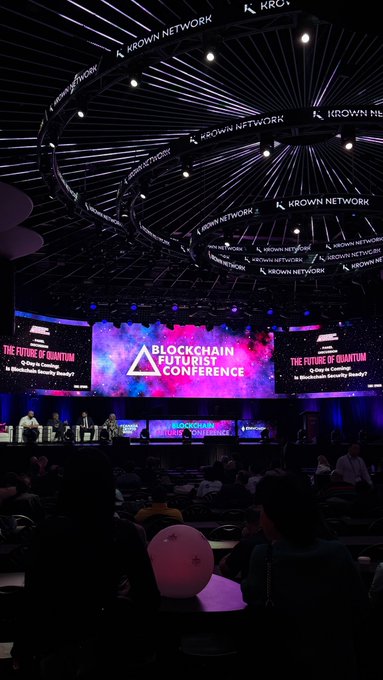 Wide shot of a large auditorium hosting the 'Blockchain Futurist Conference', with 'Krown Network' branding on the ceiling rings and screens reading 'The Future of Quantum' sponsored by Krown Network.