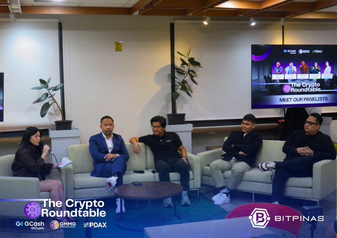A panel discussion at 'The Crypto Roundtable' featuring five seated speakers, with a screen displaying 'MEET OUR PANELISTS' and the event's sponsor logos (GCash, GMNG, PDAX, BitPinas).