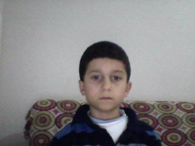 A young boy with a serious, somber expression sits on a patterned couch. His understated reaction mirrors the disappointment of cashing out only $45 from a $3,000 investment, capturing the feeling of a small return after a big risk.