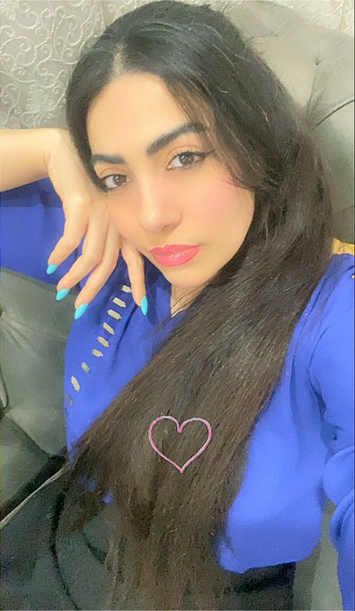 A selfie of a woman with long dark hair, wearing a blue top, with a pink heart drawn over her chest.