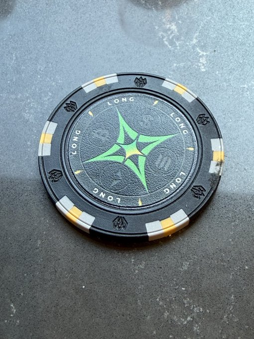 A customized poker chip styled as a Bitcoin token features the word "LONG" printed around its edge alongside a glowing green Bitcoin "₿" emblem at the center, sitting on a dark stone surface. The chip's design directly reflects the poster's bullish sentiment ("I'm long") toward Bitcoin and the traders @allinbitcoin_ and @XohebS.