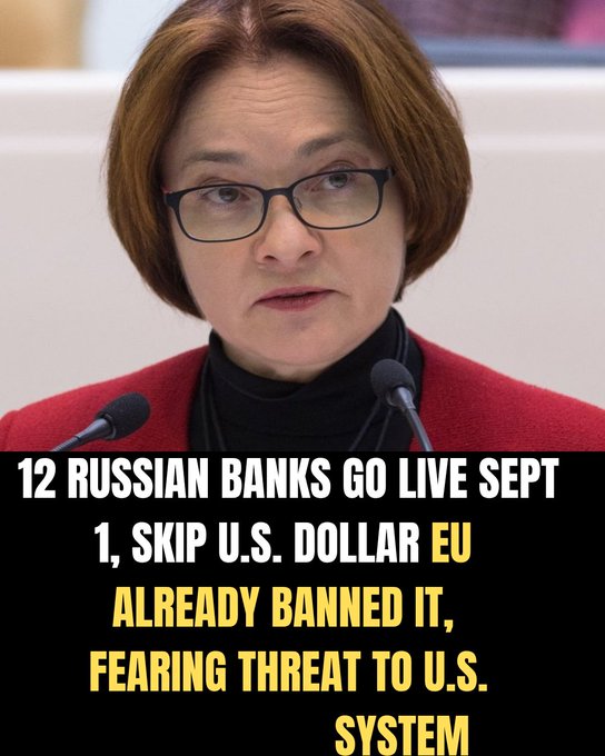A close-up of a woman with short reddish-brown hair and glasses wearing a red jacket, with bold text overlay reading '12 RUSSIAN BANKS GO LIVE SEPT 1, SKIP U.S. DOLLAR EU ALREADY BANNED IT, FEARING THREAT TO U.S. SYSTEM'.